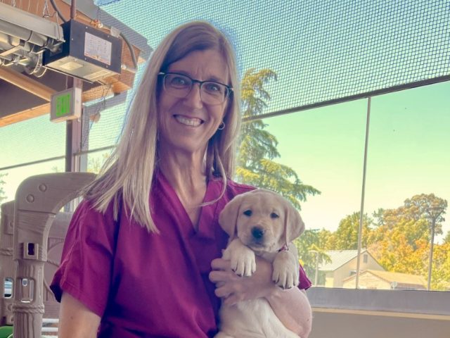 A smiling woman holds a puppy.