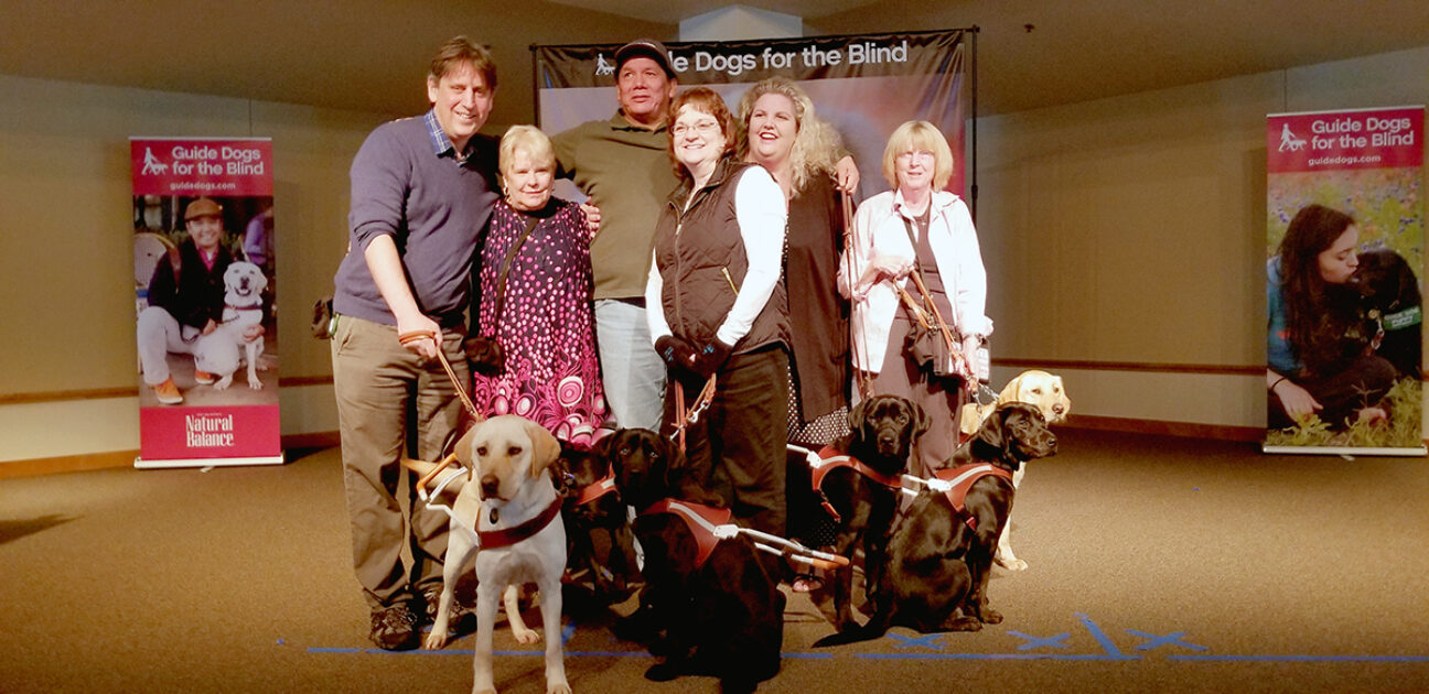 A group of people and their guide dogs share a group hug.