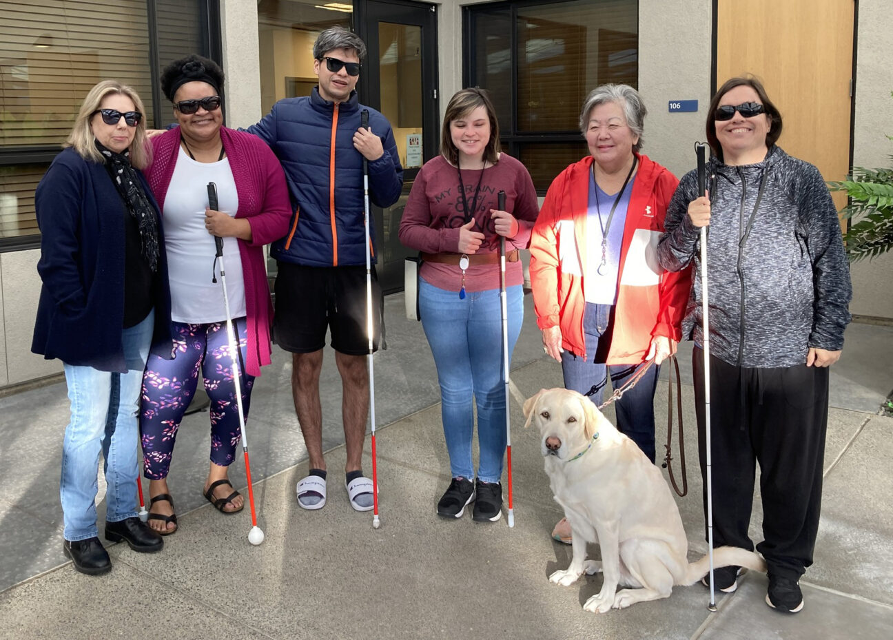 A group photo of people with white canes and one yellow Labrador Retriever.