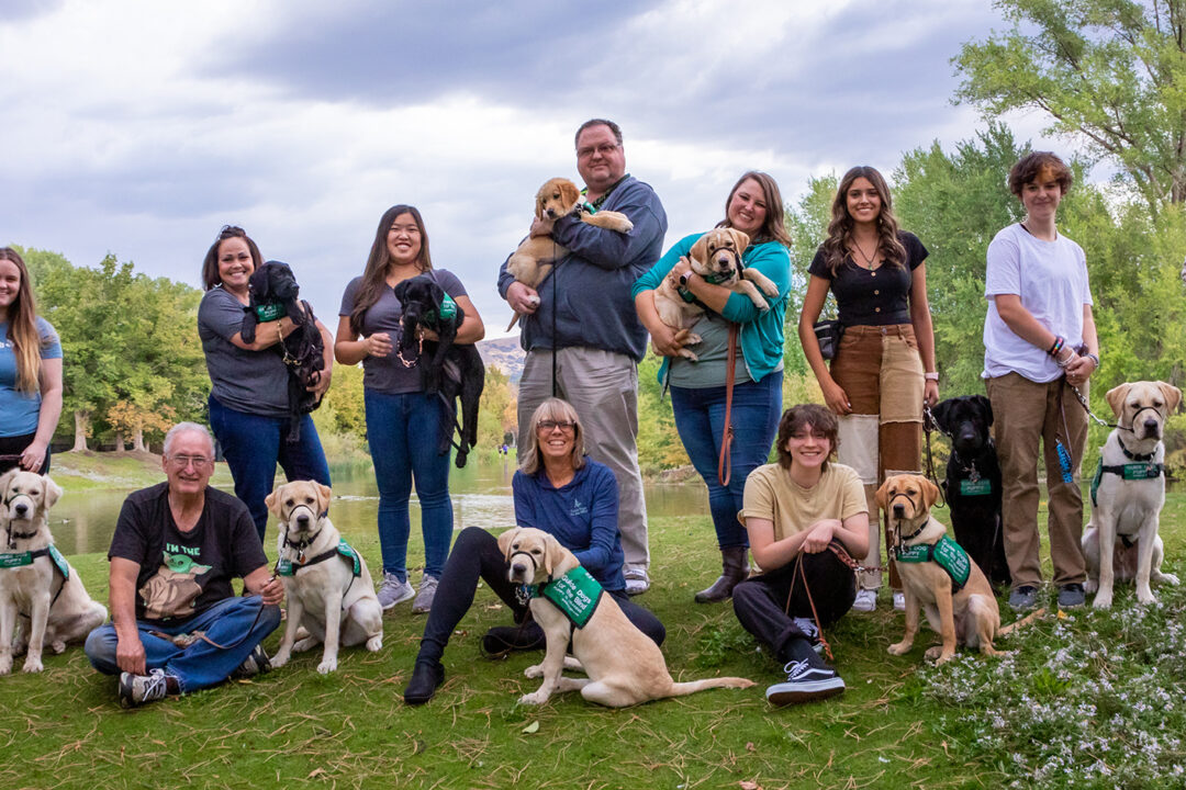 A large group of volunteer puppy raisers pose for a group photo with the puppies they are raising.