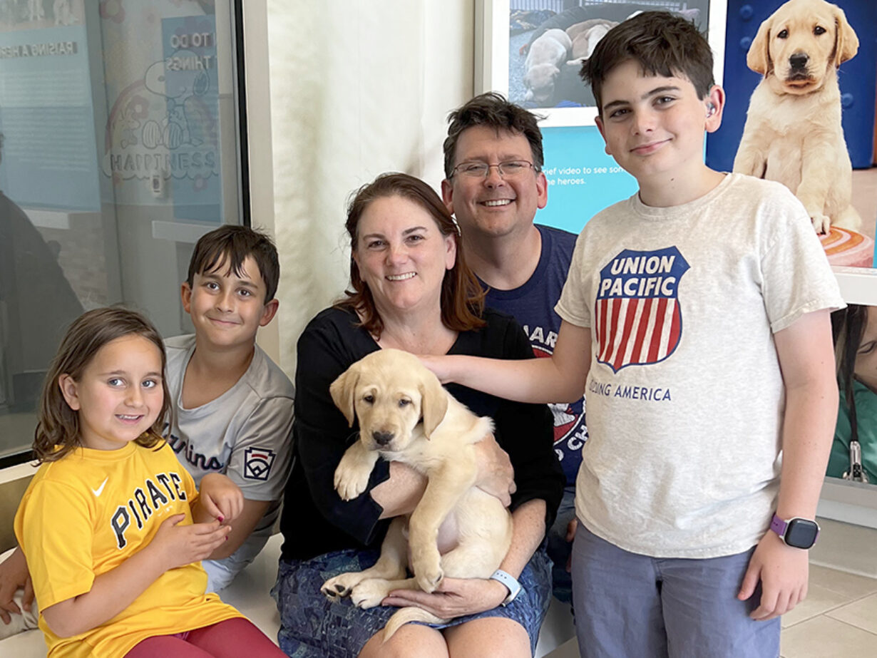 A family of five pose for a photo with a baby yellow Lab puppy.