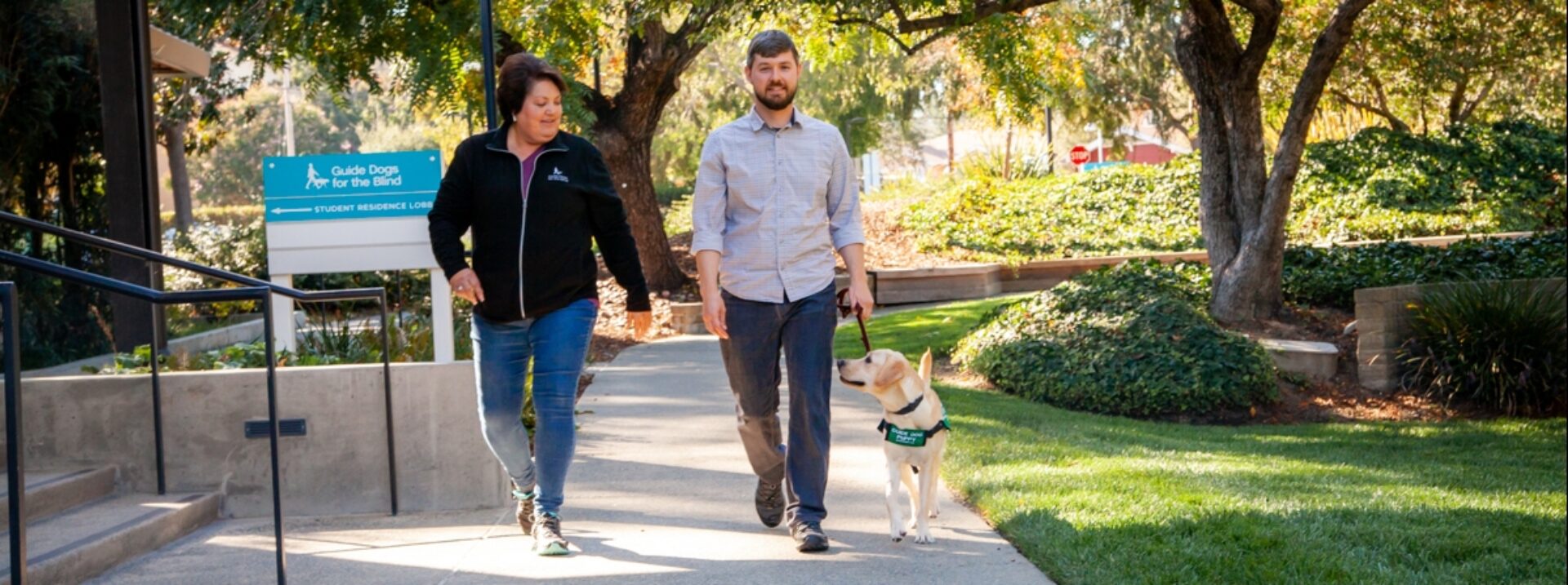 A puppy raising community field representative walking with a puppy raiser and guide dog puppy.