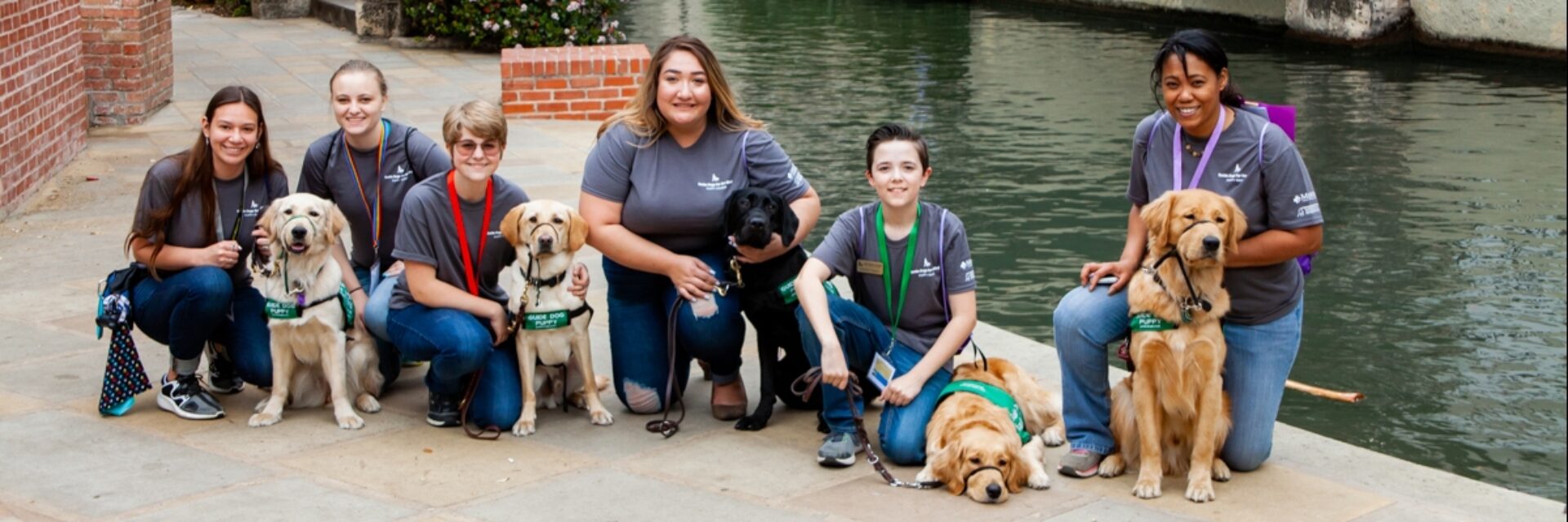 A group of six puppy raisers kneeling next to the guide dog puppies that they are raising.