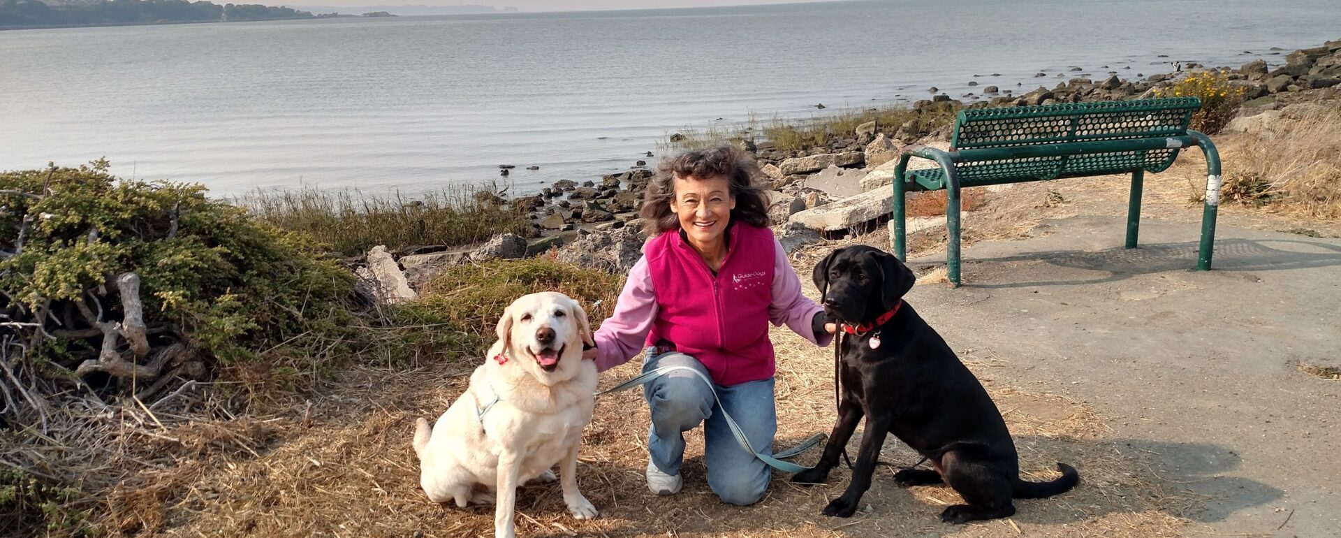 A woman poses with two dogs in front of a water view.