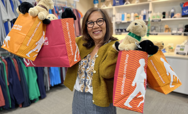 Gift shop volunteer, Laura holds bags full of GDB goodies in her arms inside the campus gift shop.