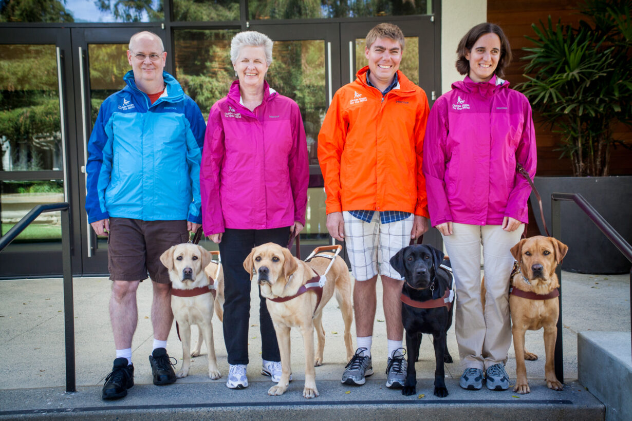 Four people with guide dogs wear colorful rain jackets.