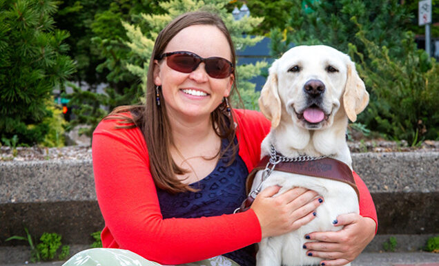 A woman embraces a yellow Lab guide dog.