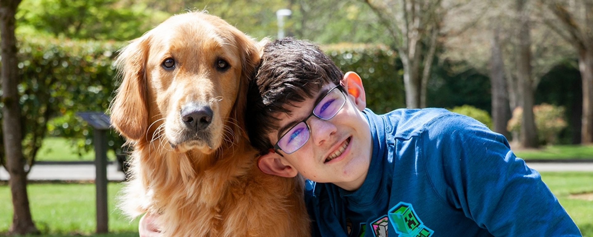 A teenage boy sitting next to his Golden Retriever K9 Buddy dog