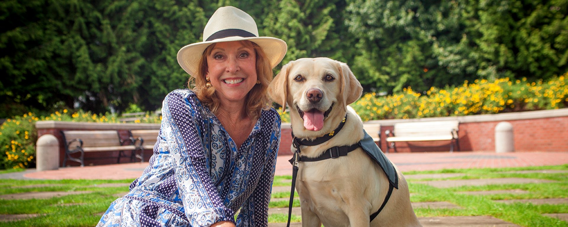 A woman wearing a hat smiles while sitting next to her yellow Lab career change dog