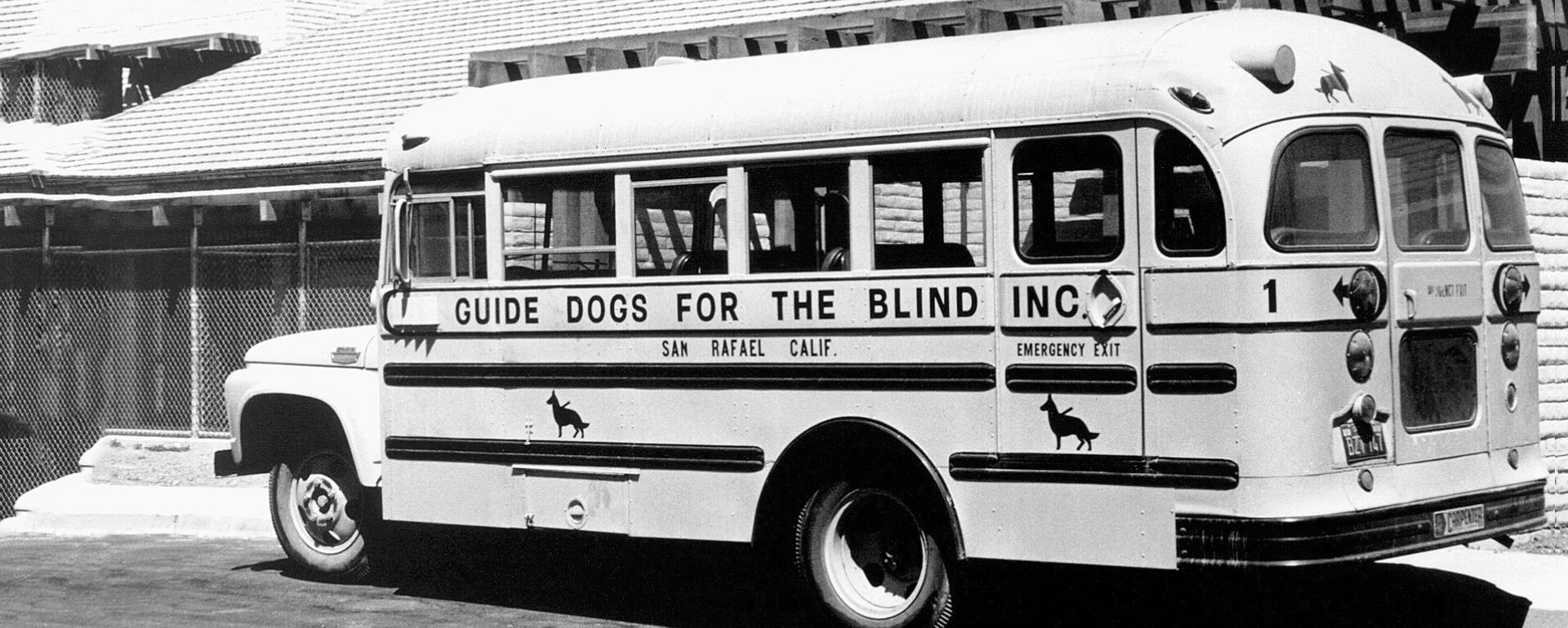 Black & white image of an old school bus that reads "Guide Dogs for the Blind - San Rafael, CA" on the side with the old shepherd logo