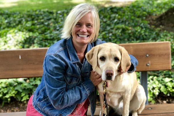 Senior Philanthropic Gifts Officer Karleanne Rogers sitting on a bench next to a yellow Labrador Retriever.