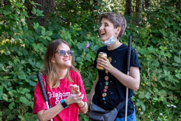 A candid moment of two people holding white canes laughing