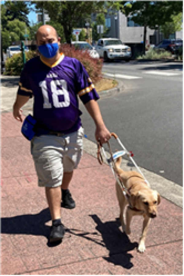 Dimitrios walks down a street with his guide dog Cami