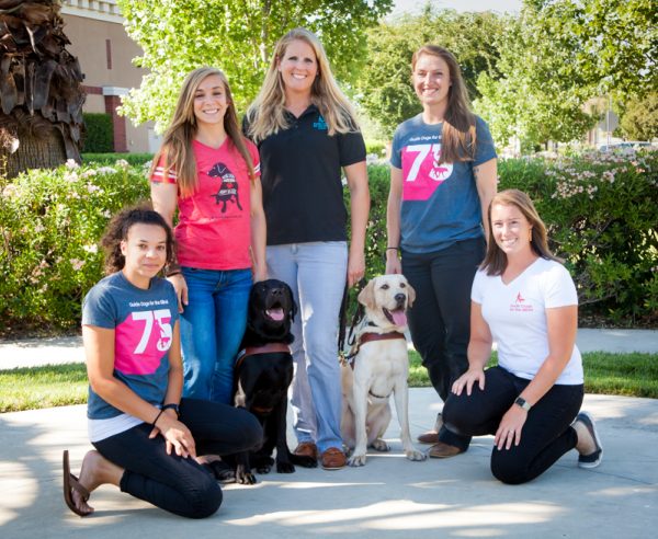 GDB's five new guide dog mobility instructors: Jessie St. Clair, Amanda Baumgartner, Palmer Dooley, Addie Yake, and Jane Allman, with two guide dogs in harness (one black Lab and one yellow Lab).