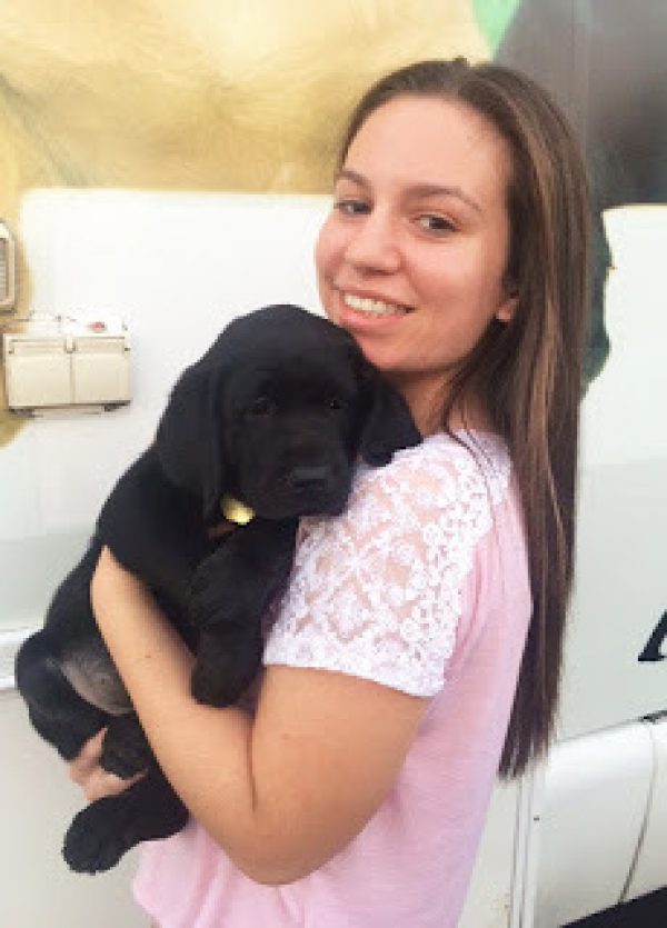 Jaclyn in a pink shirt holding a black Lab puppy.