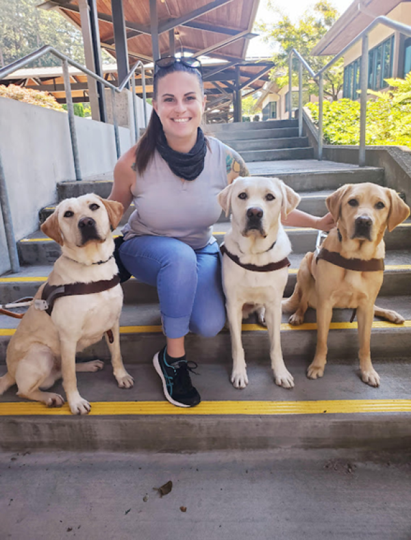 Shelby Gelormo sits next to three guide dogs in training.