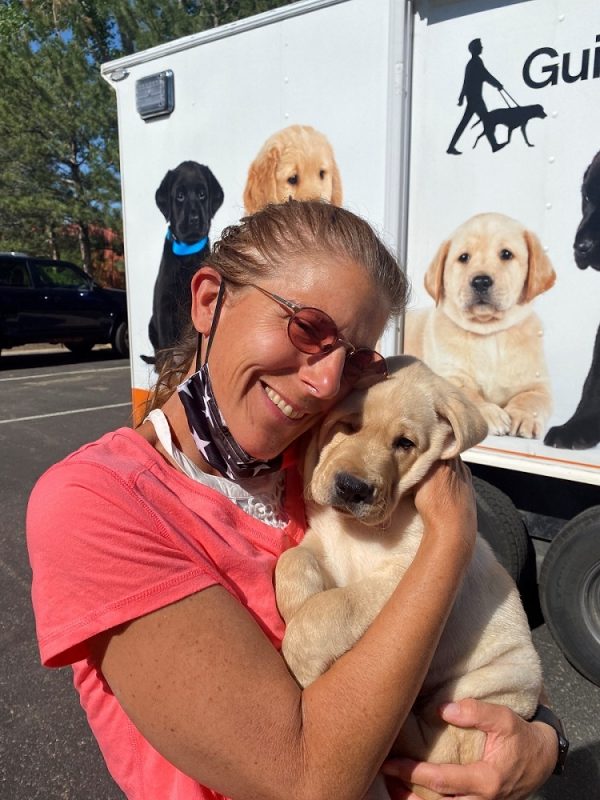 Puppy raiser Wendy Davis smiles as she holds a yellow Lab puppy in front of the puppy truck