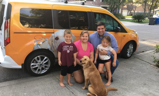 A family - mom, dad, and two kids - in front of a GDB vehicle with their K9 Buddy.
