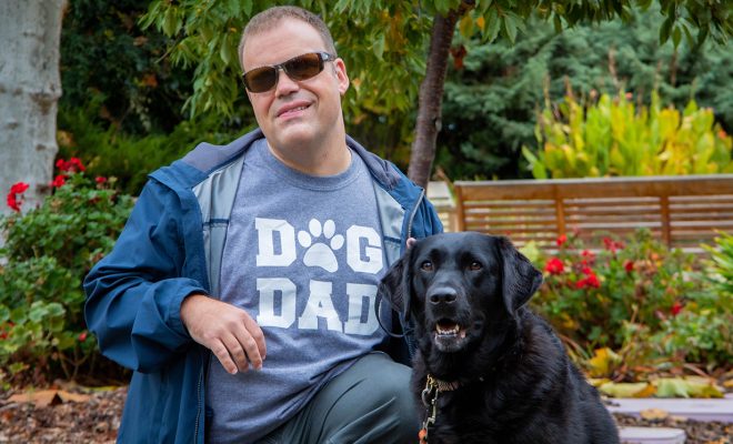 A man with a black Lab K9 Buddy dog.
