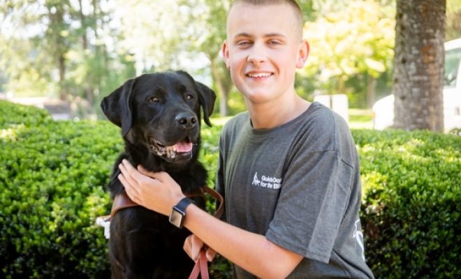 A young boy sitting next to a black Lab guide dog.